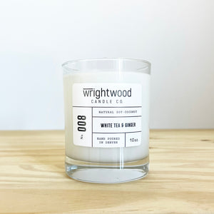 Container candle in a clear glass jar sitting on wood table with a white background. White label with black text states the company name (Wrightwood Candle Co), scent name, what it is made out of (soy-coconut wax), where it is hand poured (Denver) and item weight (10oz.)