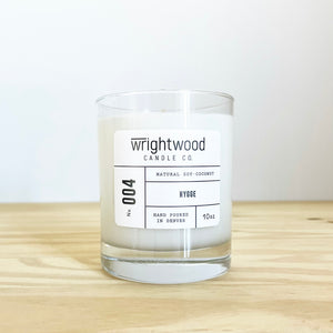 Container candle in a clear glass jar sitting on wood table with a white background. White label with black text states the company name (Wrightwood Candle Co), scent name, what it is made out of (soy-coconut wax), where it is hand poured (Denver) and item weight (10oz.)