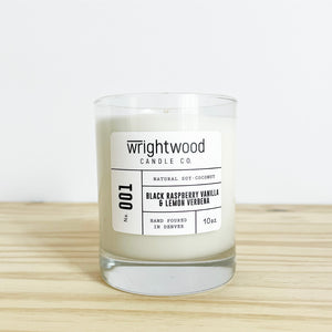 Container candle in a clear glass jar sitting on wood table with a white background. White label with black text states the company name (Wrightwood Candle Co), scent name, what it is made out of (soy-coconut wax), where it is hand poured (Denver) and item weight (10oz.)