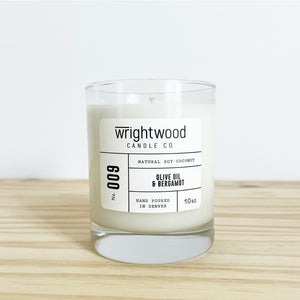 Container candle in a clear glass jar sitting on wood table with a white background. White label with black text states the company name (Wrightwood Candle Co), scent name, what it is made out of (soy-coconut wax), where it is hand poured (Denver) and item weight (10oz.)