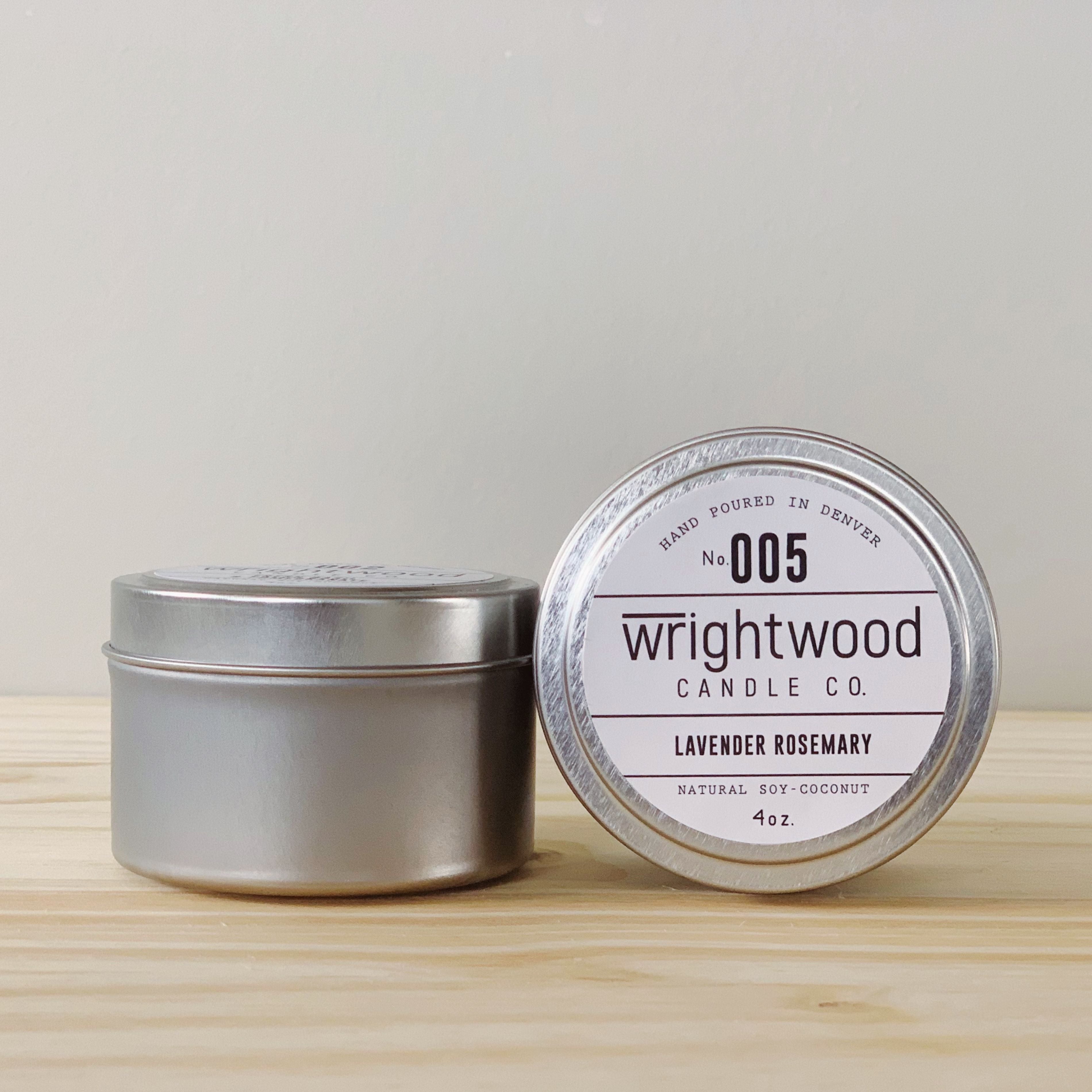 Two silver tins are on a wood table with a light colored background. The one on the left is upright while the one on the right has the lid facing outward with label visible. The label states the company name (Wrightwood Candle Co), scent name, what it is made out of (soy-coconut wax), where it is hand poured (Denver) and item weight (4oz.)
